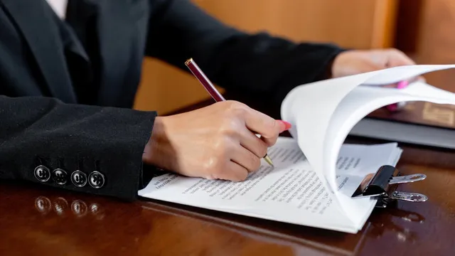 Pessoa revisando e assinando documentos jurídicos importantes em ambiente profissional de advocacia